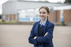 Student stood with folded arms smiling in front of academy building