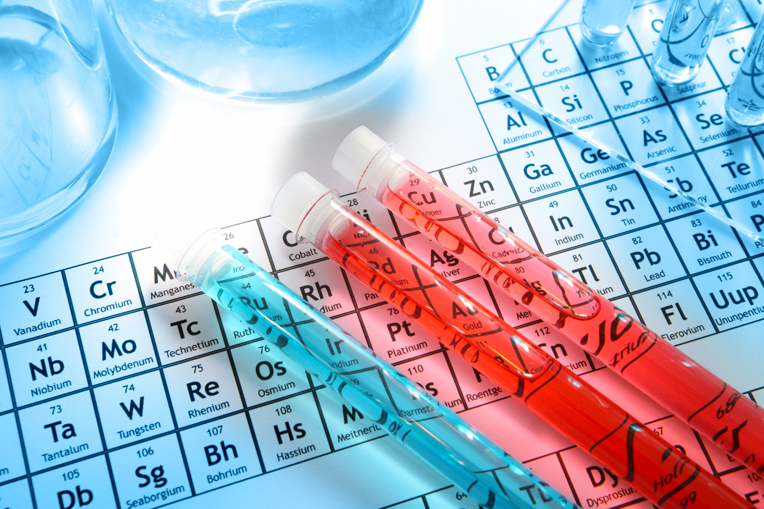 Chemistry research laboratory with glass equipment, test tubes with red liquid on periodic table background showing chemical elements. Selective focus. Light blue background.