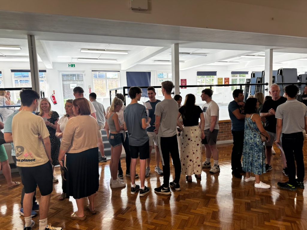 Several Post-16 students are seen gathered together in an atrium in the academy building, whilst they open their A-Level results.